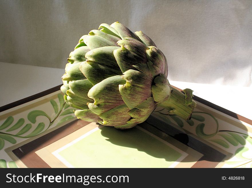 Still life of an artichoke sitting on a plate.