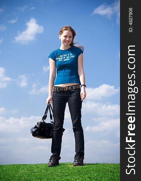 The young attractive girl with a handbag on a background of the blue sky