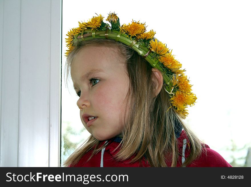 A girl in front of the window wearing dandelion wreath on her head. A girl in front of the window wearing dandelion wreath on her head