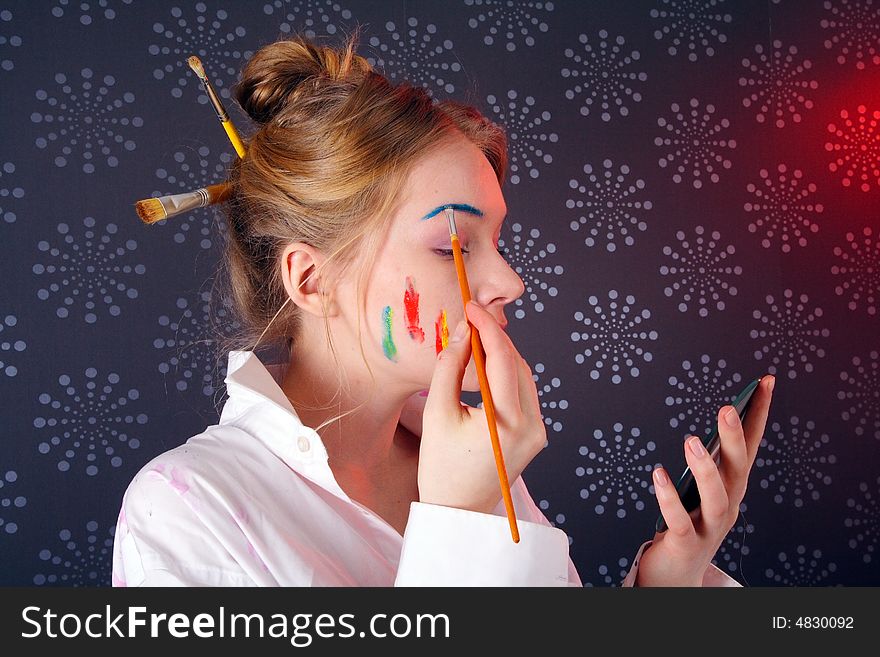 Beautiful young woman putting paint on her face as makeup. Beautiful young woman putting paint on her face as makeup