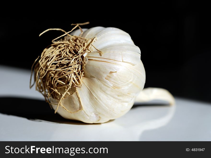 A garlic bulb placed on creamic kitchen shelf with black background