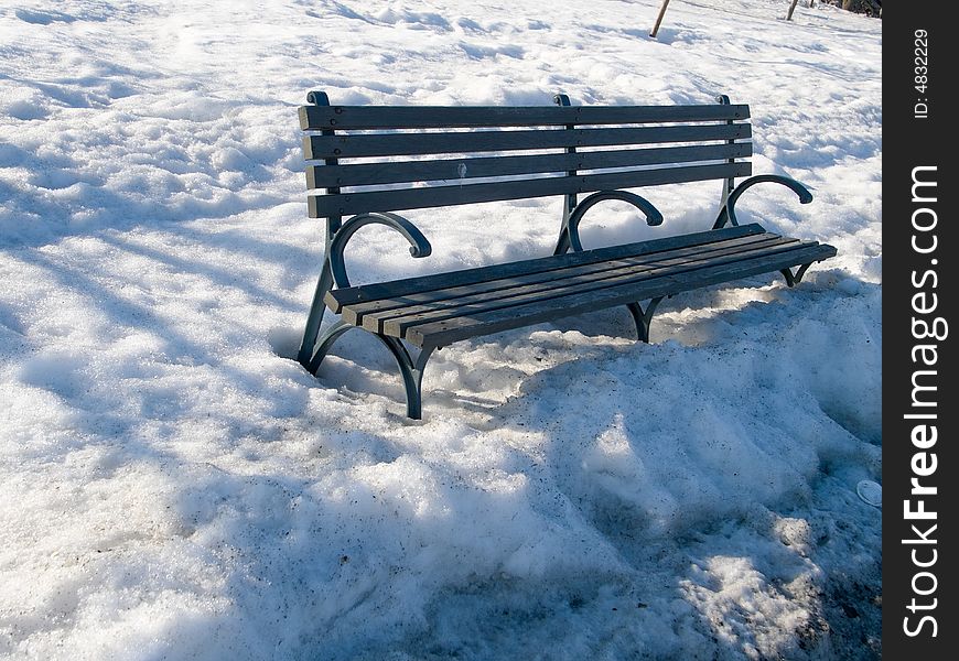 Park bench in the thawing snow at sunset