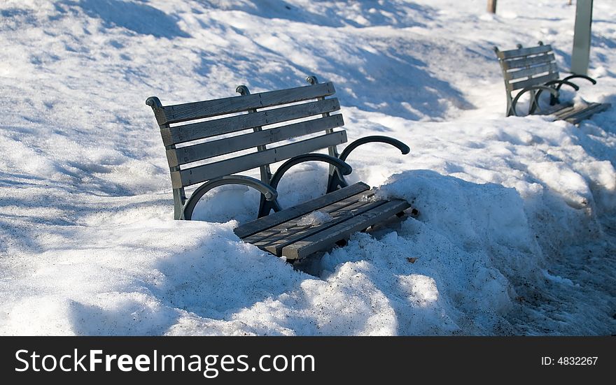 A row of park benches in the thawing snow at sunset