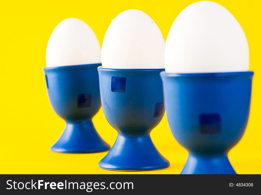 Three white eggs in blue egg cups (focus on middle egg)