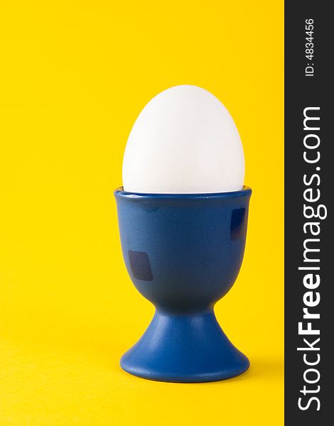 White egg in a blue egg cup on a yellow background