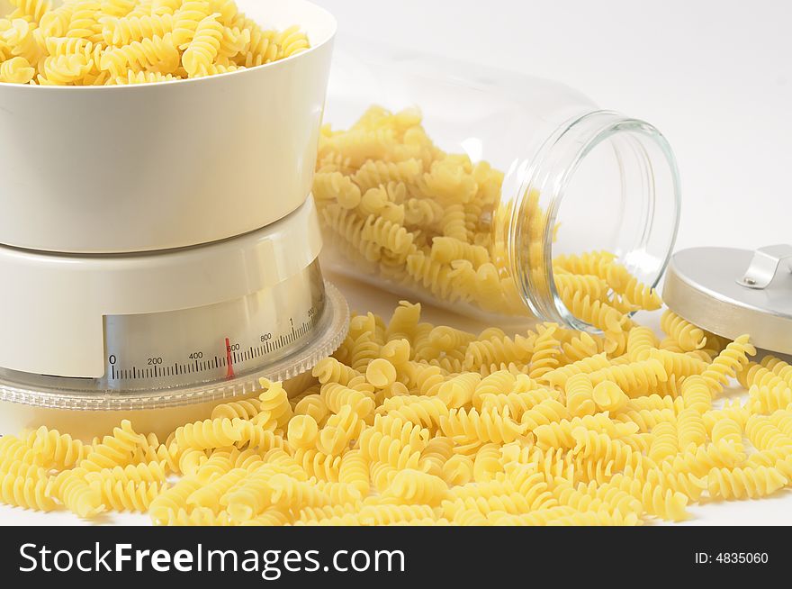 Italian fusilli pasta falling out of a glass jar and a balance