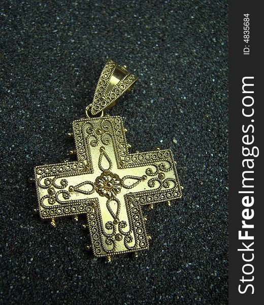 Antique golden cross jewel lying in black sand
