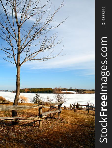 A fence leading to a frozen lake under a blue sky. A fence leading to a frozen lake under a blue sky