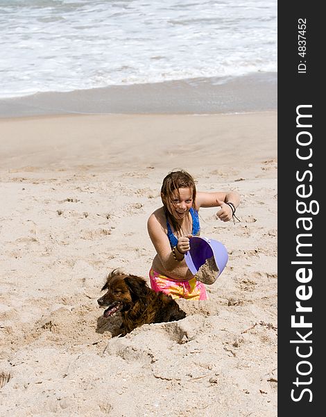 Young girl playing on the beach in the sand with a purple bucket and her dog. Young girl playing on the beach in the sand with a purple bucket and her dog