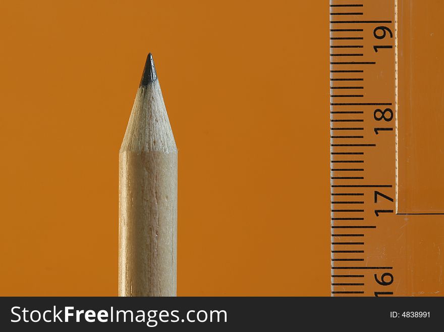 A pencil and a ruler with a simple  orange color background. A pencil and a ruler with a simple  orange color background