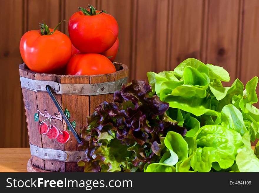 Lettuce and tomatoes in bucket against wooden background. Lettuce and tomatoes in bucket against wooden background