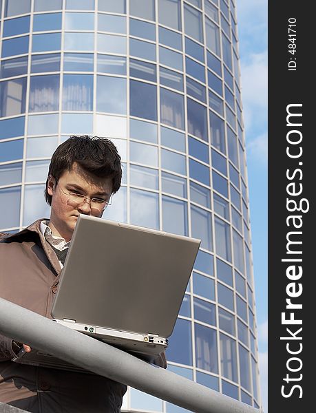 Young concentrated businessman with laptop on the building background