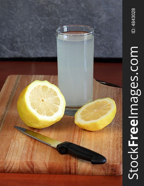 A glass of lemon on a cutting board with a piece of lemon and a knife. A glass of lemon on a cutting board with a piece of lemon and a knife.