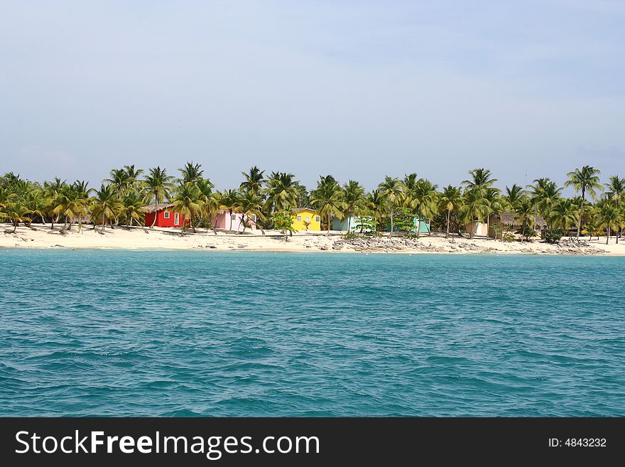 Caribbean white sand beach with palm trees andvibrantly coloured,wooden houses. Caribbean white sand beach with palm trees andvibrantly coloured,wooden houses.