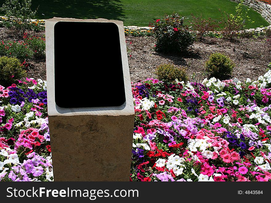 A blank black sign  ready for text sits in a flower bed with lots of colors. A blank black sign  ready for text sits in a flower bed with lots of colors.