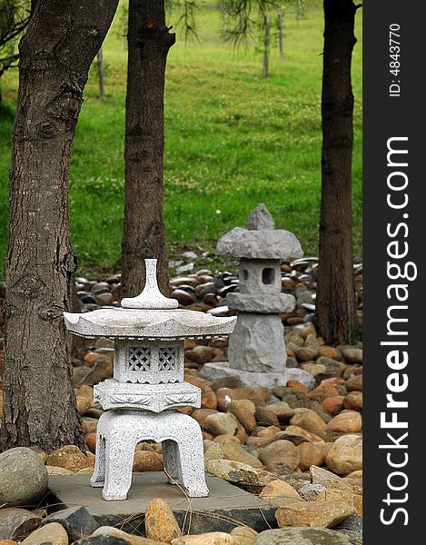 Small buddhist sculptures made of stone, small stones, green grass, and trees in background. Small buddhist sculptures made of stone, small stones, green grass, and trees in background
