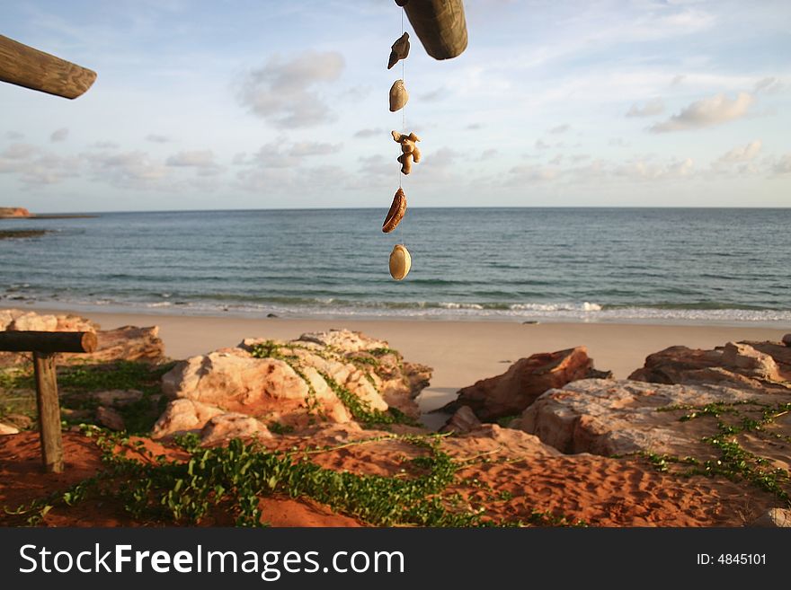 Hanging shells on a string with red rocks and sandy beach in background. Cape Leveque, The Kimberley. Australia