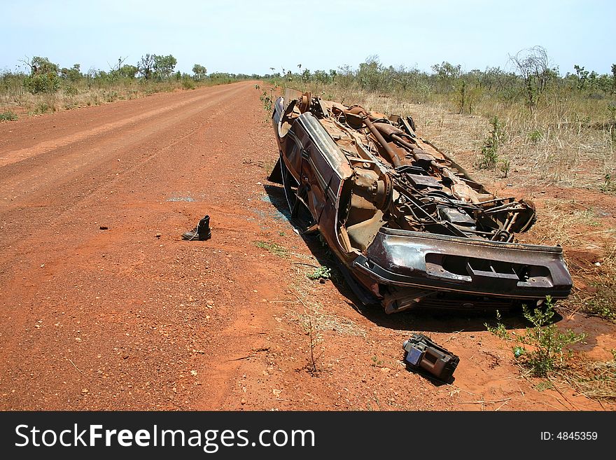 Australian red rural road with an overturned obsolete rusted car on the roadside. Tanami road, Western Australia. Australian red rural road with an overturned obsolete rusted car on the roadside. Tanami road, Western Australia