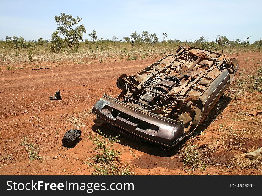 Australian red rural road with an overturned obsolete rusted car on the roadside. Pollution Damage. Tanami road, Western Australia. Australian red rural road with an overturned obsolete rusted car on the roadside. Pollution Damage. Tanami road, Western Australia