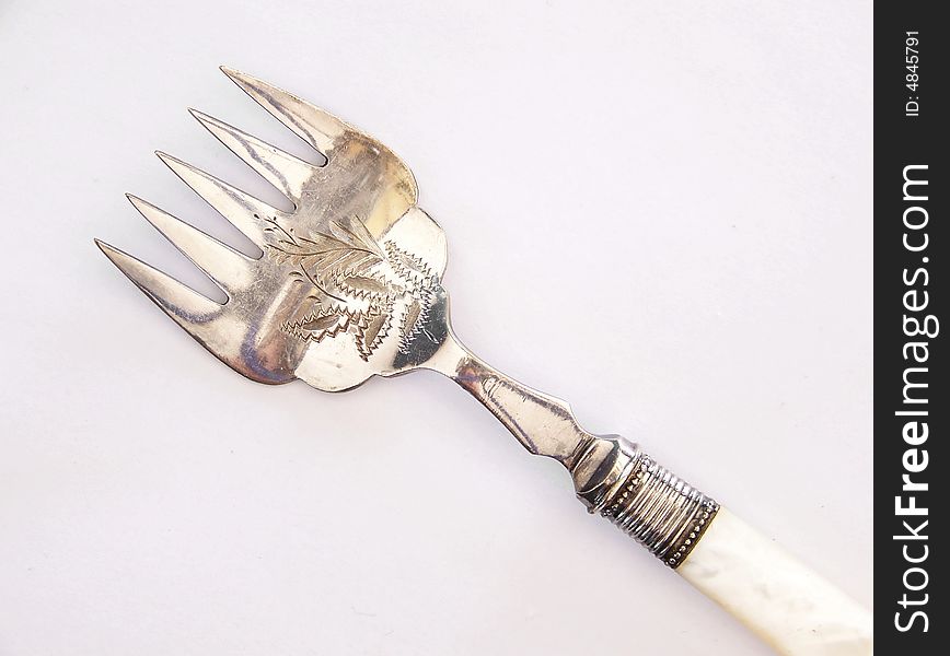 Image of an antique pickle fork with intricate design. Horizontal orientation.