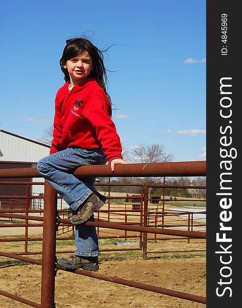 Pretty little girl sitting on metal fence by outdoor arena. Pretty little girl sitting on metal fence by outdoor arena.