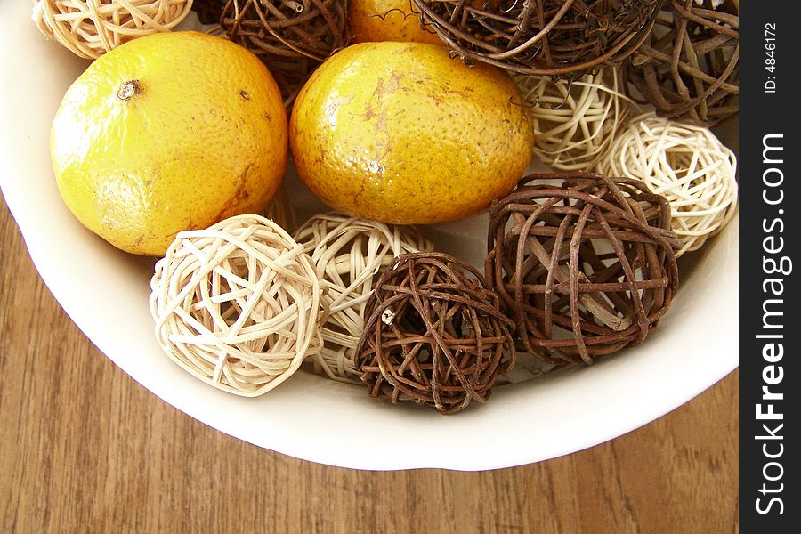 Image of honey tangerines and vine decorations mixed together in a white bowl on a wooden table.  Horizontal orientation.