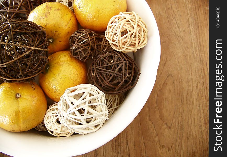 Image of honey tangerines and vine decorations mixed together in a white bowl on a wooden table, set to the left of the image.  Horizontal orientation.