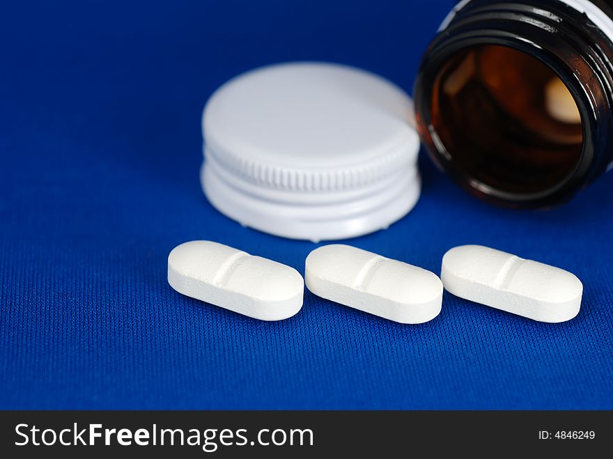 Close up to three pills infront of bottle and lid on blur background. Close up to three pills infront of bottle and lid on blur background