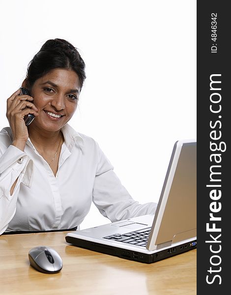 Indian business woman smiling on her cell phone while working at her laptop. Isolated against a white background. Indian business woman smiling on her cell phone while working at her laptop. Isolated against a white background