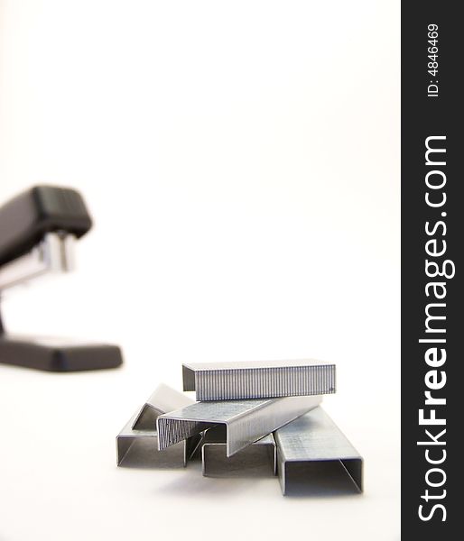 Image of staple refills in foreground, with black stapler in background. Vertical orientation. Image of staple refills in foreground, with black stapler in background. Vertical orientation.