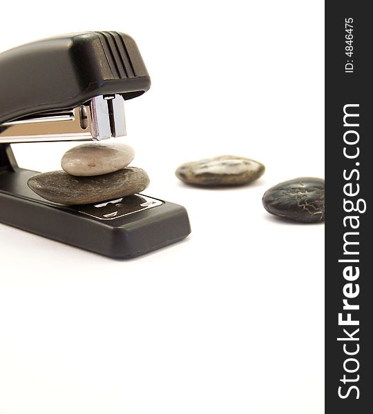 Image of a black stapler about to staple two stones together.  Other stones are nearby.  Vertical orientation. Image of a black stapler about to staple two stones together.  Other stones are nearby.  Vertical orientation.