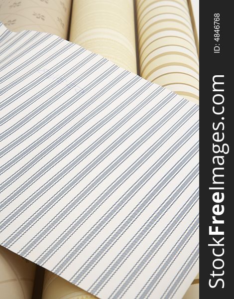 Close up of blue striped wall paper swatch on top of three beige wall paper rolls. Close up of blue striped wall paper swatch on top of three beige wall paper rolls.