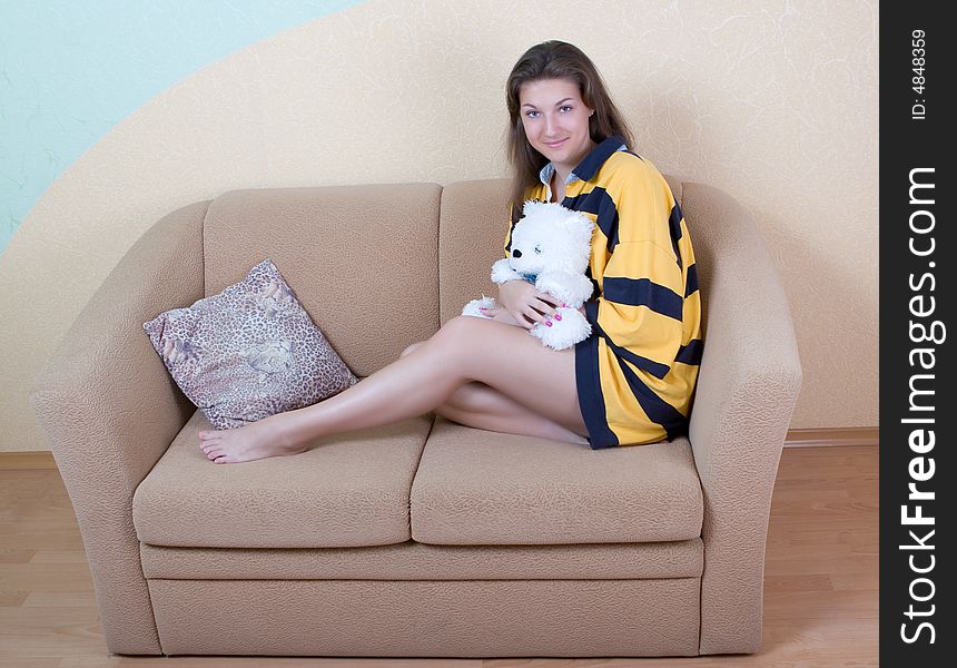Attractive girl sits on a sofa with a toy bear