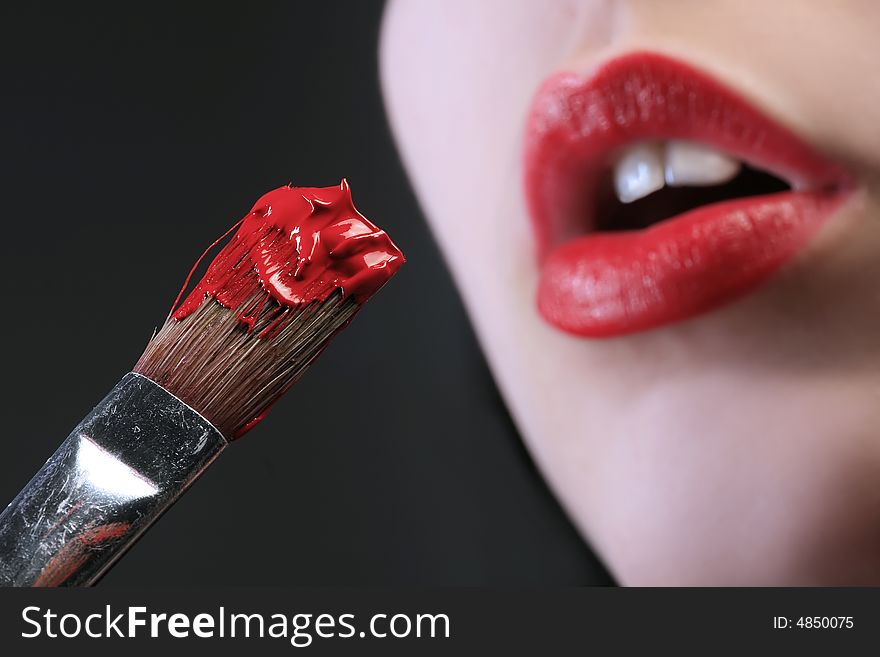 A brush with paint and red lips in background