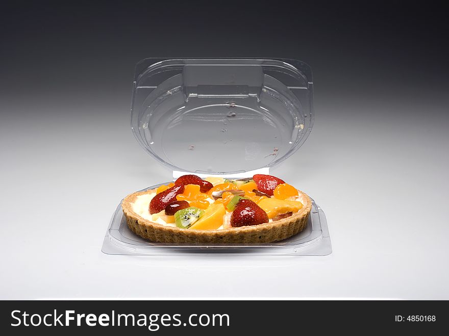 A fruit pie in a plastic transparent box on a gray to white background