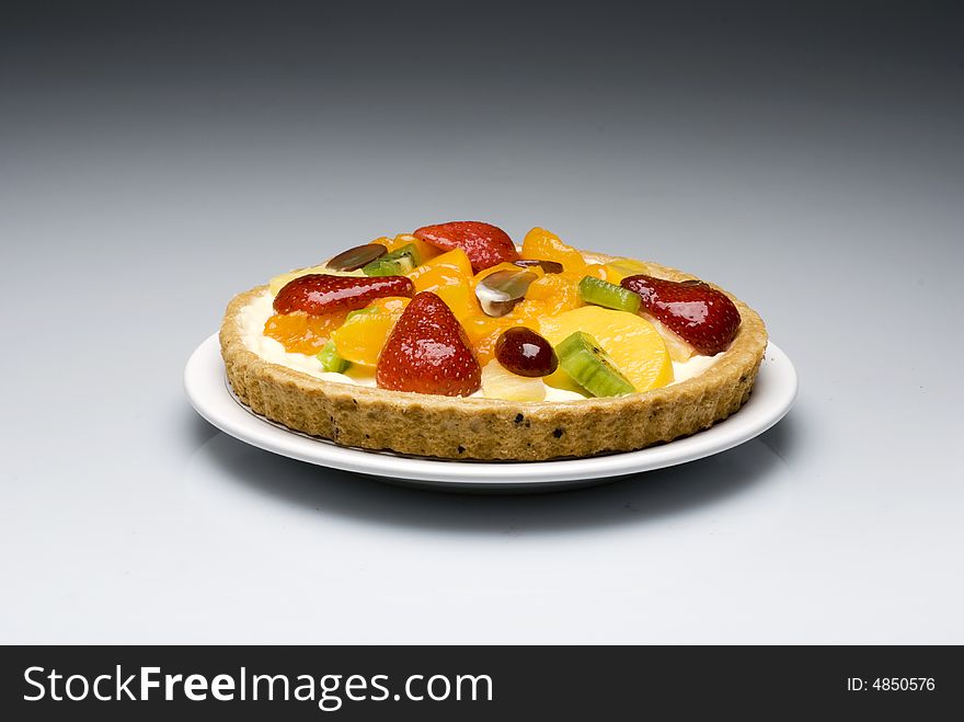 A fruit pie in a plastic transparent box on a gray to white background