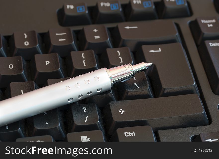 A silver pen lying on a computer keyboard. A silver pen lying on a computer keyboard