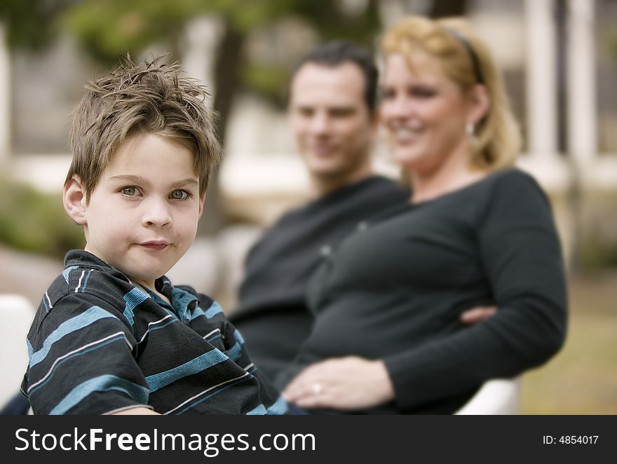 Little boy in the foreground smiles with his mom and dad in the background. Little boy in the foreground smiles with his mom and dad in the background