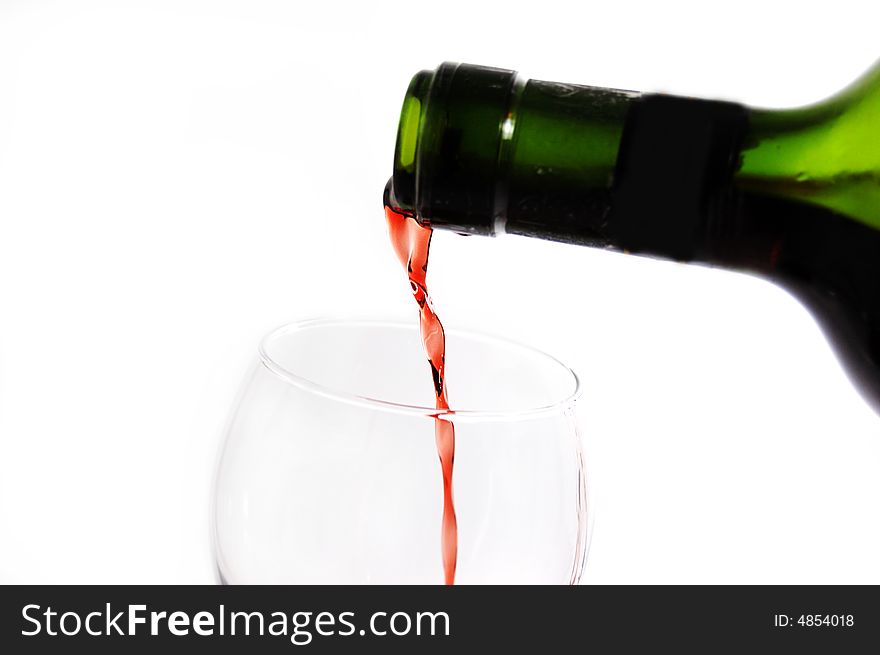 Green bottle pouring red wine into wineglass over white