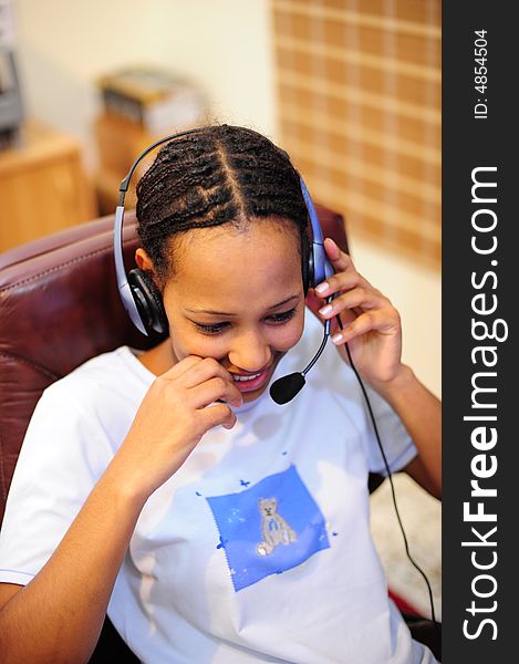 Pretty African girl relaxing on a chair, talking over a headset and smiling. DOF is very shallow and focus is on the eyes only. Pretty African girl relaxing on a chair, talking over a headset and smiling. DOF is very shallow and focus is on the eyes only