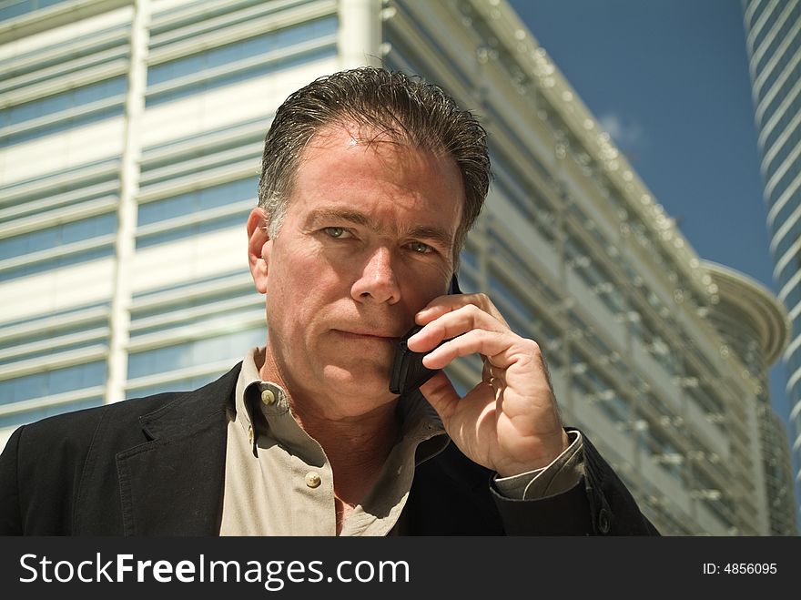 A man on a cell phone with high rise office buildings in the background. A man on a cell phone with high rise office buildings in the background.