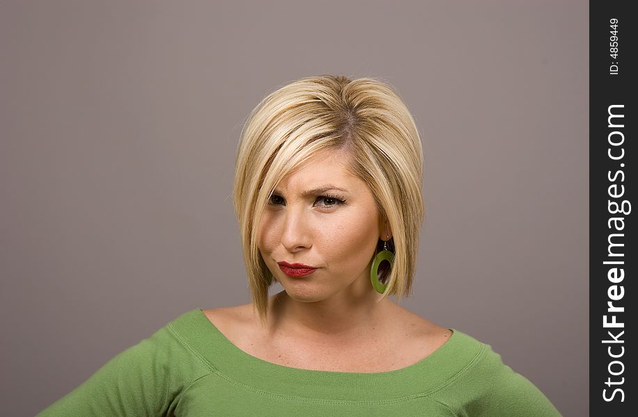 A blonde in green blouse on grey background with a stern or disapproving look. A blonde in green blouse on grey background with a stern or disapproving look