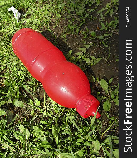 Thrown plastic bottle of red color on  background of  grass