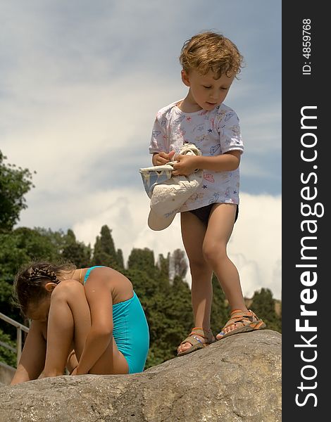 A little boy in a sport shirt stands on a stone on a background mountains and gets on the hip a service cap. A little boy in a sport shirt stands on a stone on a background mountains and gets on the hip a service cap