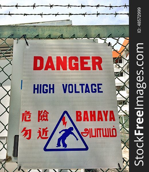 A warning sign outside an electric power supply station fenced with barbed wires. The languages displayed are English, Mandarin, Malay and Tamil. A warning sign outside an electric power supply station fenced with barbed wires. The languages displayed are English, Mandarin, Malay and Tamil.