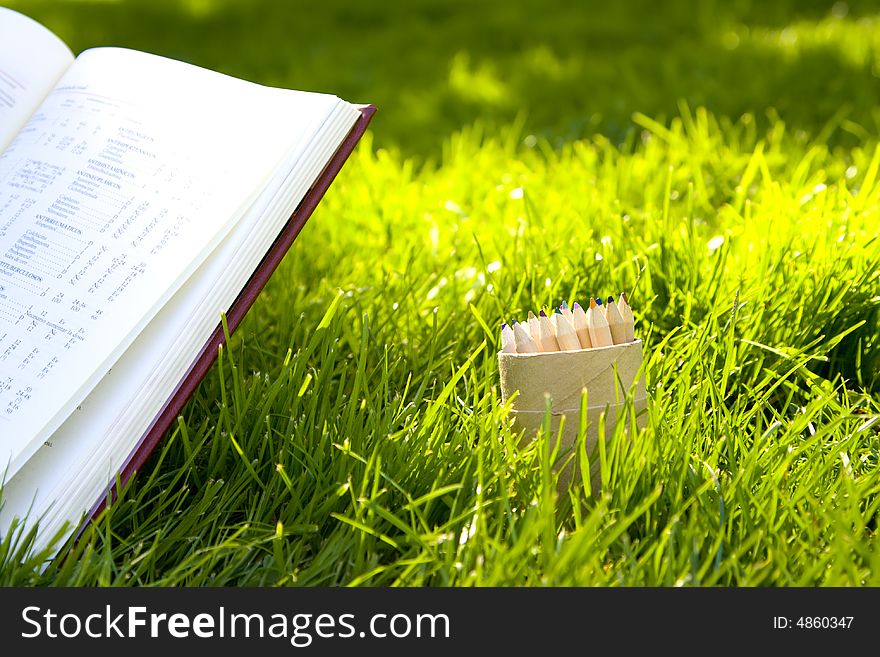 Multicolored pencilsand opened book over green background. Multicolored pencilsand opened book over green background.