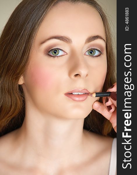 Young woman with green eyes and long brown hair getting her make-up done by a make-up artist � lip liner application. Young woman with green eyes and long brown hair getting her make-up done by a make-up artist � lip liner application