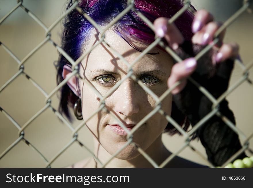 Young woman with colorful hair behind a chain link fence. Young woman with colorful hair behind a chain link fence