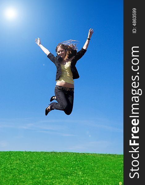 The young jumping girl with headphones on a background of the blue sky