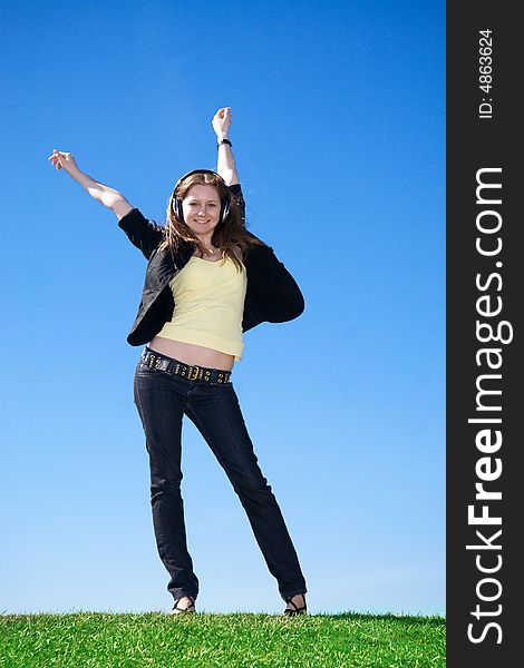 The young attractive girl with headphones on a background of the blue sky